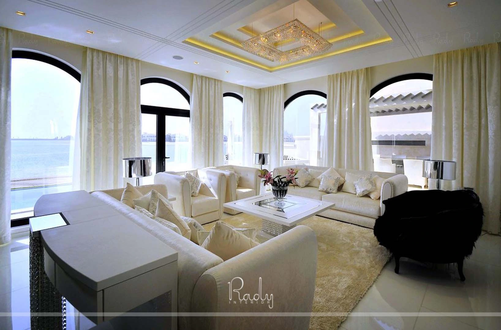 A renovated villa living room in Palm Jumeirah featuring white furniture and large windows, designed by Rady Interior.